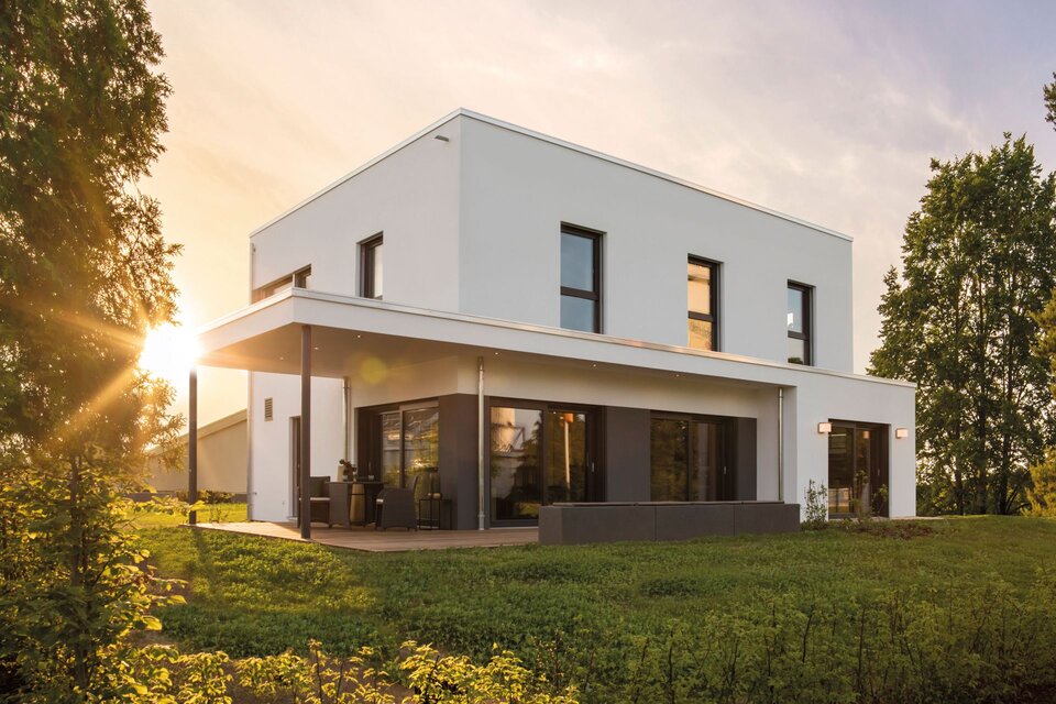 Modernes Flachdachhaus ALTERO mit überdachter Terrasse und klarer Fassadengestaltung im Abendlicht, Musterhaus Gießen.