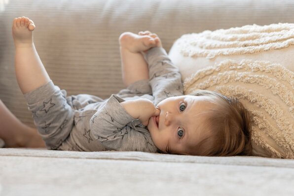 Baby liegt entspannt auf einem Sofa und schaut in die Kamera
