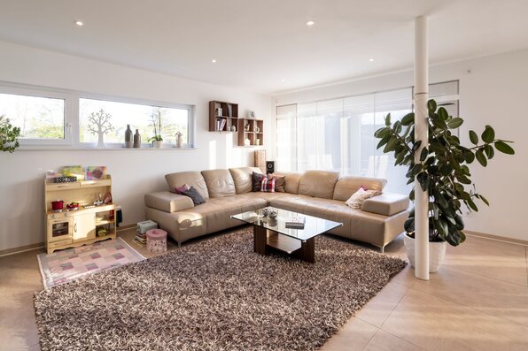 Gemütliches Wohnzimmer in einem FingerHaus mit großer Ledercouch, Glastisch, Kinder-Spielküche und dekorativen Pflanzen.