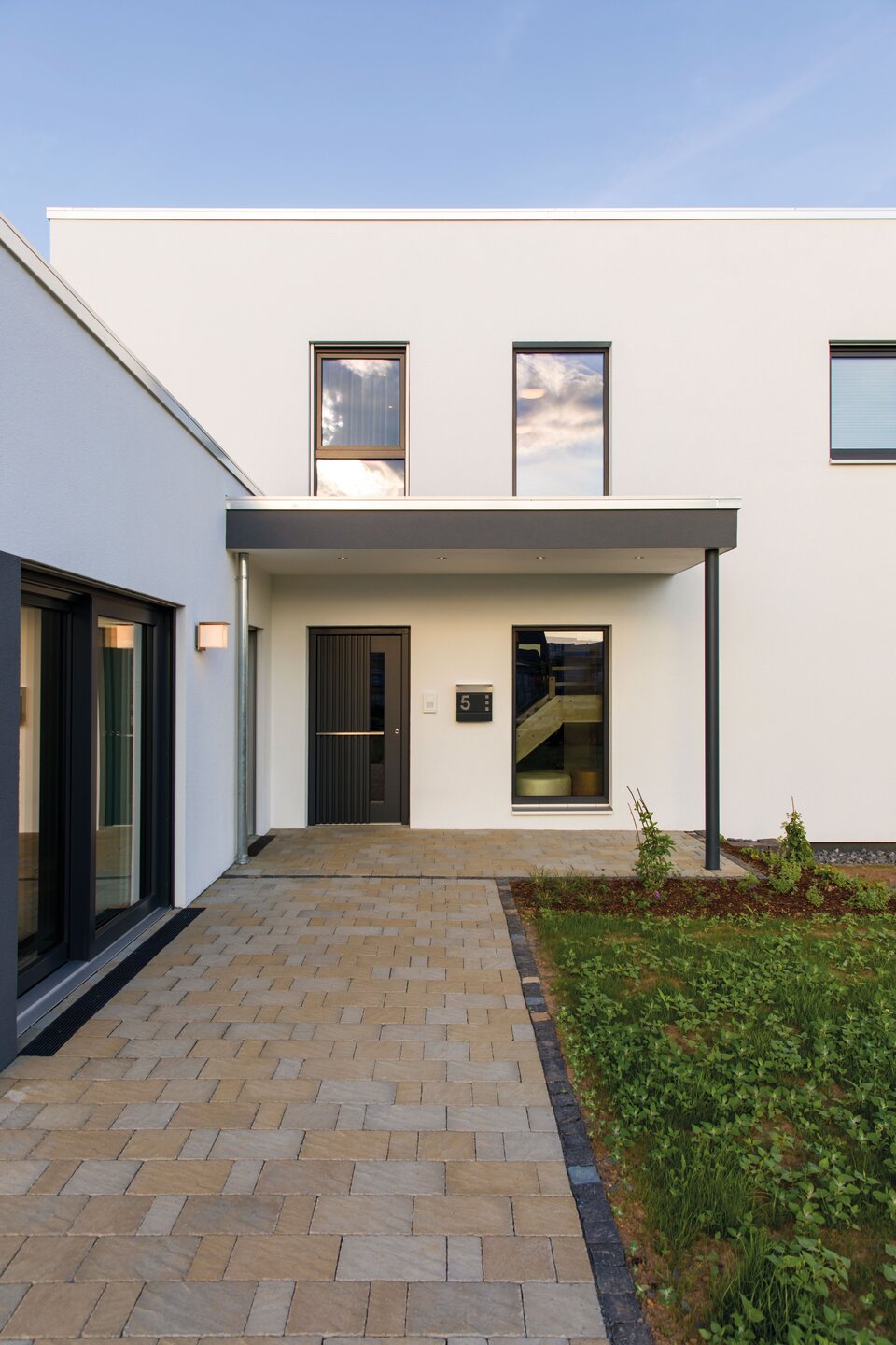 Eingangsbereich des FingerHaus Musterhauses ALTERO in Gießen mit moderner geradliniger Architektur, überdachtem Eingang und gepflastertem Weg.