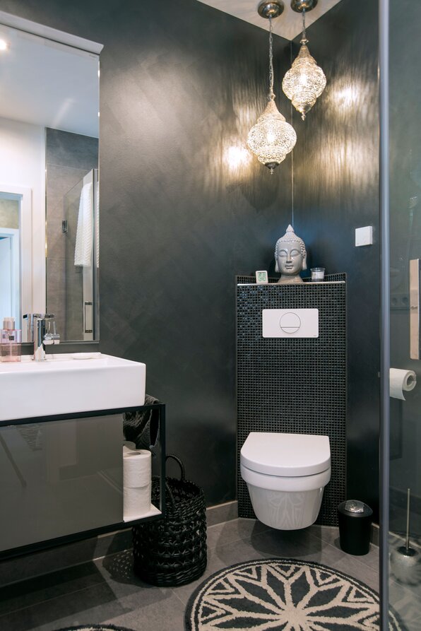 Modern gestaltetes Gäste-WC in einem FingerHaus NIVO 130 mit dunkler Wandgestaltung, Wand-WC, Waschtisch, dekorativen Hängelampen und Buddha-Figur.