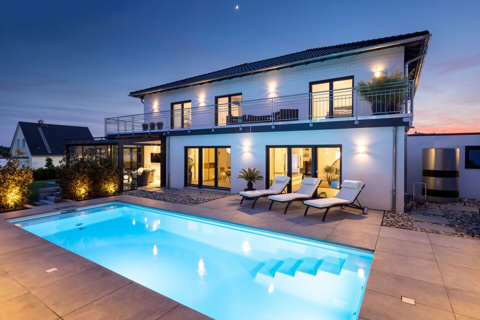 Frei geplantes Finger-Haus mit großem Pool, beleuchteter Terrasse und moderner Architektur in der Abenddämmerung.