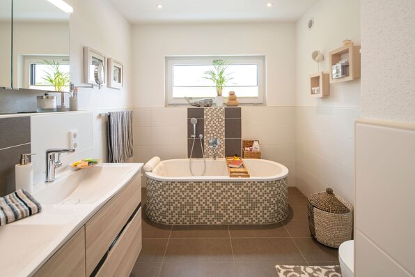 Modernes Badezimmer in einem frei geplanten FingerHaus mit Mosaik-Badewanne, Doppelwaschbecken, großen Fliesen und dekorativen Elementen.