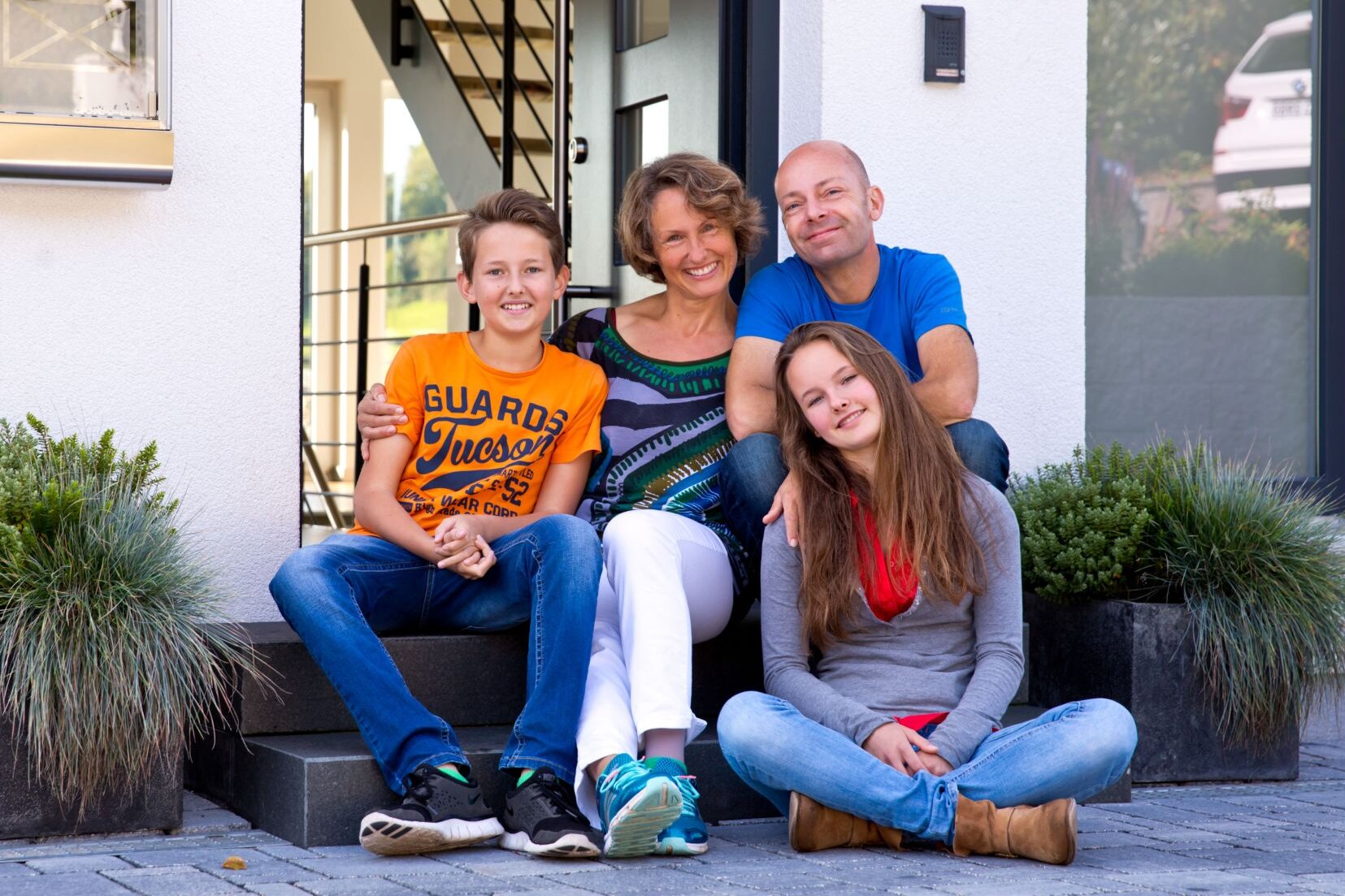 Glückliche Familie sitzt vor ihrem frei geplanten FingerHaus auf der Eingangstreppe und lächelt in die Kamera.