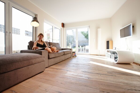 Moderner Wohnbereich mit großem Sofa, Holzfußboden und viel Tageslicht in einem frei geplanten FingerHaus.