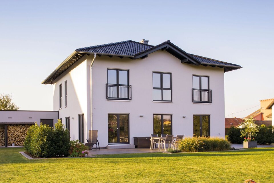 Modernes zweigeschossiges FingerHaus mit weißer Fassade, dunklem Satteldach, bodentiefen Fenstern und gepflegtem Garten mit Rasenfläche und Terrasse.