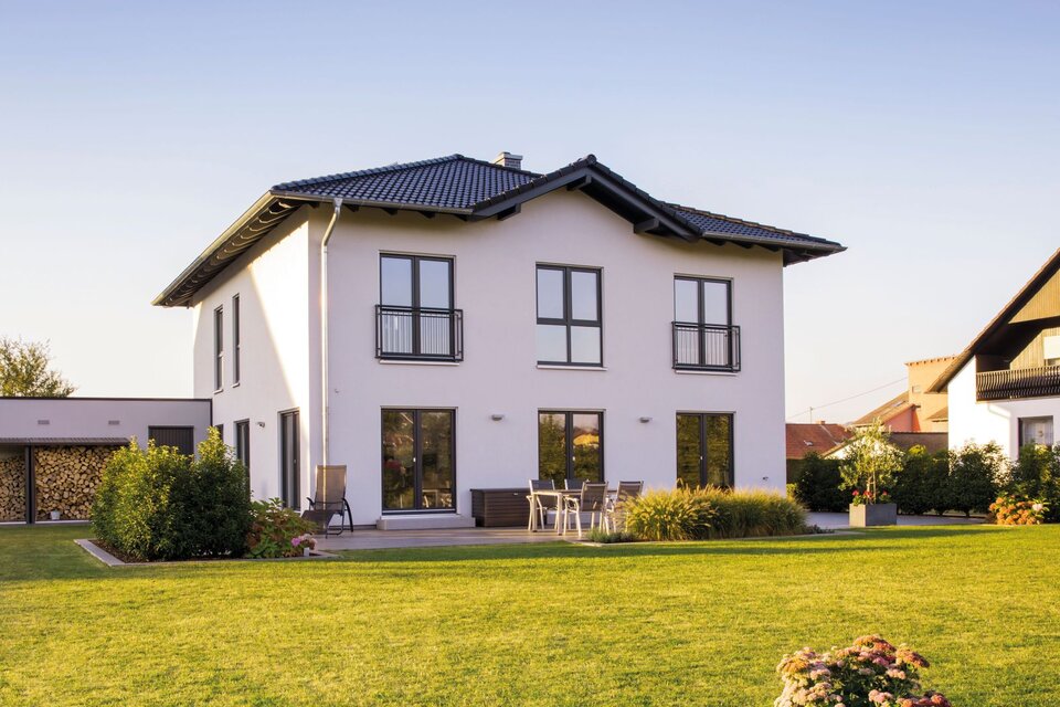 Modernes zweigeschossiges FingerHaus mit weißer Fassade, dunklem Satteldach, bodentiefen Fenstern und gepflegtem Garten mit Rasenfläche und Terrasse.