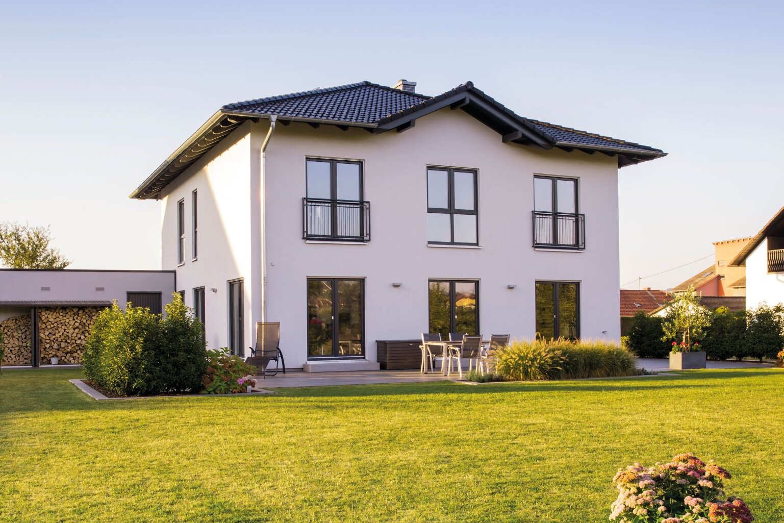 Modernes zweigeschossiges FingerHaus mit weißer Fassade, dunklem Satteldach, bodentiefen Fenstern und gepflegtem Garten mit Rasenfläche und Terrasse.