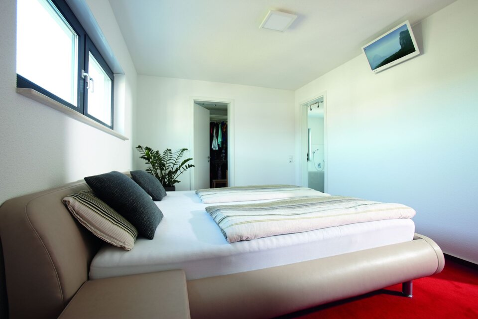 Großes Schlafzimmer mit breitem Bett, vielen Kissen und warmem Tageslicht.