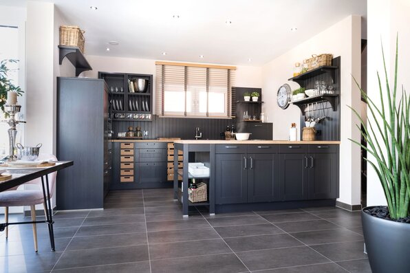 Moderne Landhausküche in dunklem Design mit Kochinsel, offenen Regalen und viel Stauraum im Musterhaus MEDLEY 300 B in Poing.
