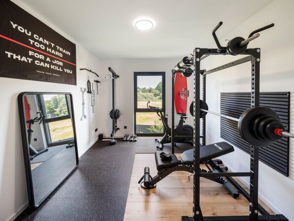 Fitnessraum im Haus mit Kraftstation, Hantelbank, Spiegel und Trainingsgeräten