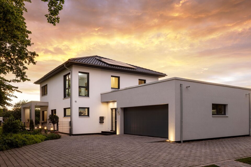 Modernes FingerHaus mit Doppelgarage bei Sonnenuntergang, beleuchtetem Eingangsbereich und gepflegtem Vorgarten.