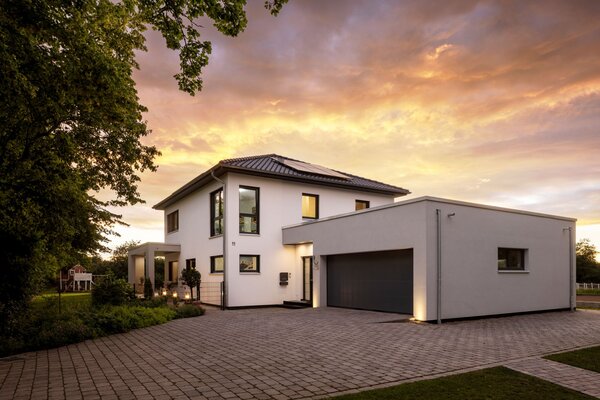 Modernes FingerHaus mit Doppelgarage bei Sonnenuntergang, beleuchtetem Eingangsbereich und gepflegtem Vorgarten.