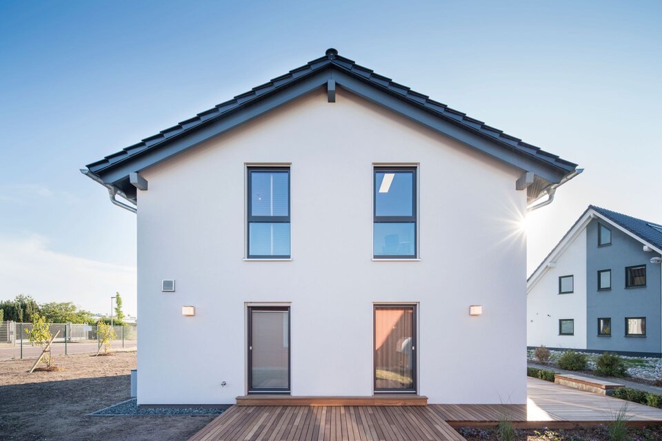 Terrassenseite des Musterhauses UNO 2.0 in Leipzig mit klarer Fassade, großen Fenstern und Holzterrasse.