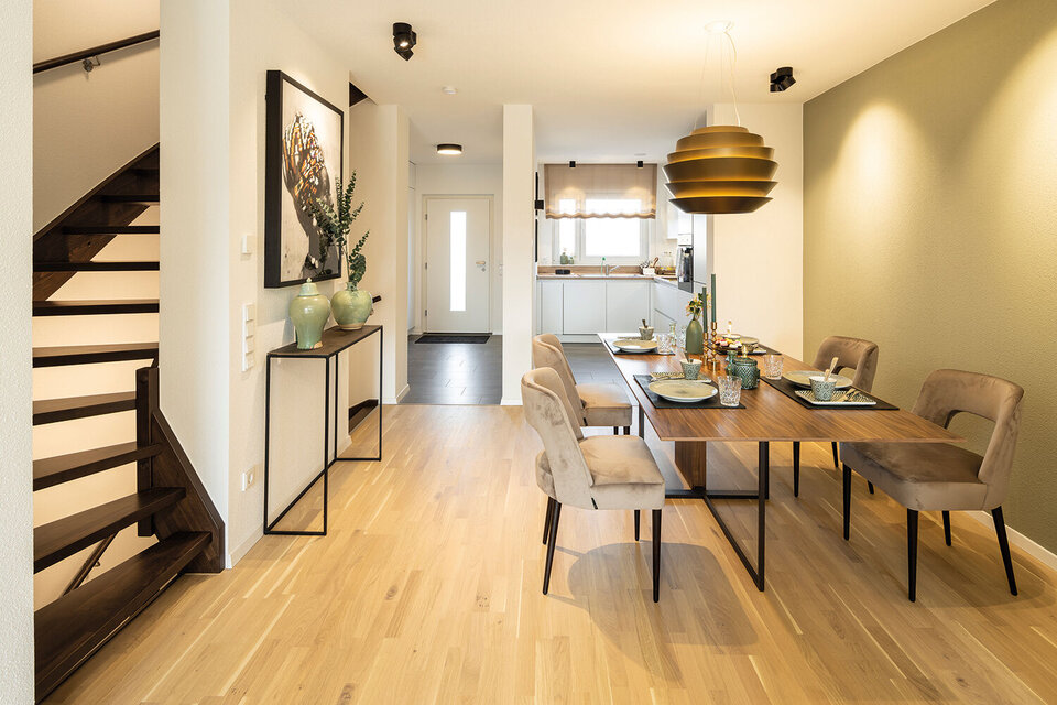 Essbereich mit Holztisch und gepolsterten Stühlen, große runde Hängelampe, angrenzender Flur mit Treppe.