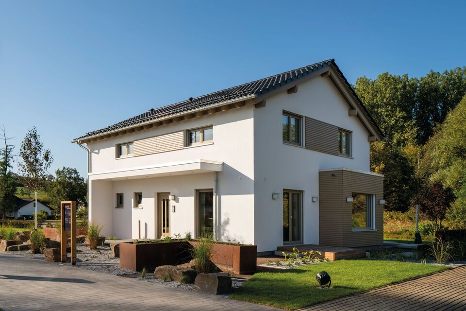Moderne zweigeschossige Hausarchitektur mit Satteldach, heller Putzfassade, großen Fenstern und gepflegter Außenanlage im Musterhaus Frankenberg.