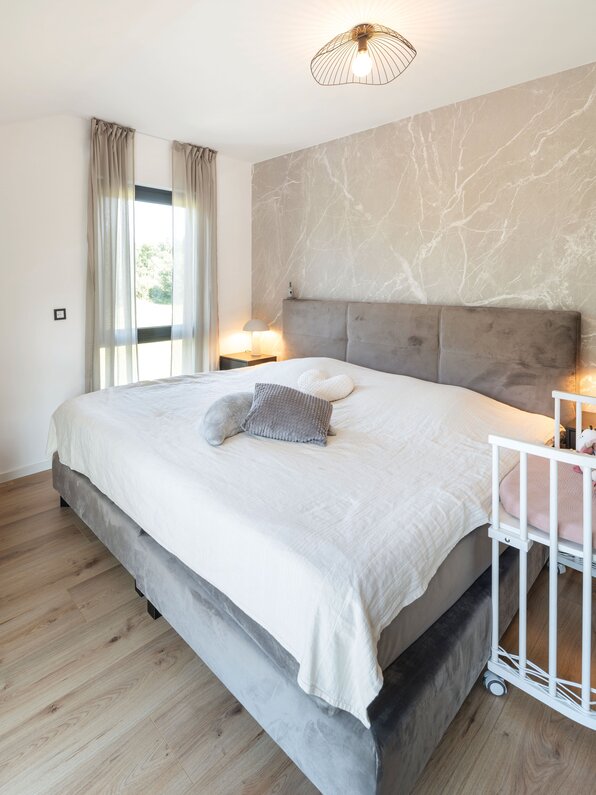 Modernes Schlafzimmer mit großem Doppelbett, gepolstertem Kopfteil und Babybett