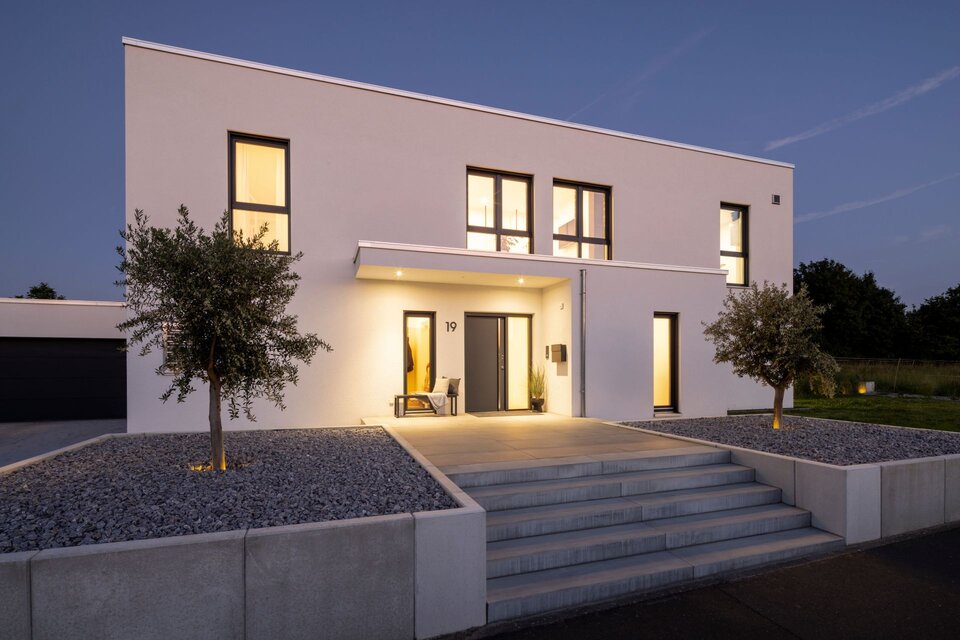 Abendliche Außenansicht eines modernen FingerHaus im Bauhaus-Stil. Beleuchteter Eingangsbereich mit breiter Treppe, klaren Linien und minimalistischer Gestaltung.