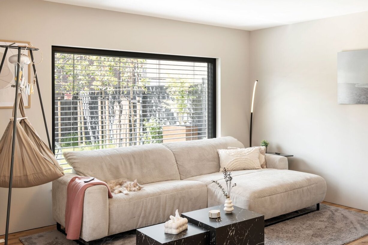 Wohnzimmer mit Sofa, Couchtischen, Teppich und großem Fenster mit Raffstores