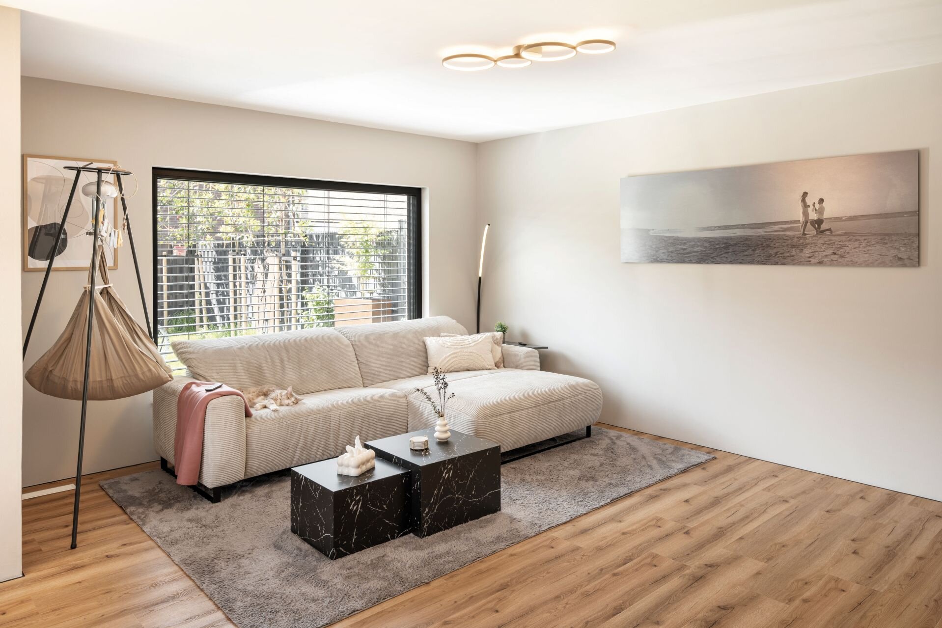 Wohnzimmer mit Sofa, Couchtischen, Teppich und großem Fenster mit Raffstores