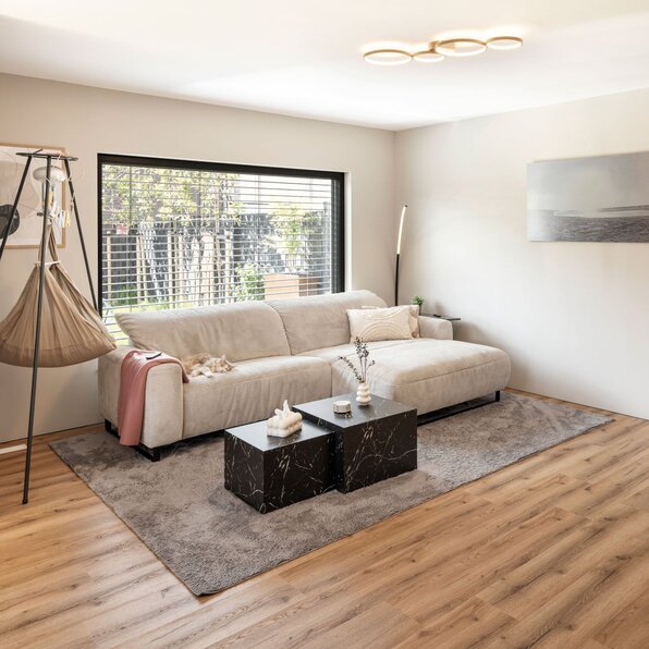 Wohnzimmer mit Sofa, Couchtischen, Teppich und großem Fenster mit Raffstores