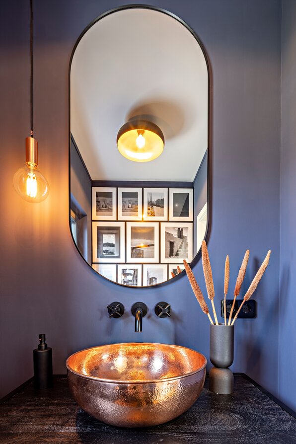 Stilvolles Gäste-Bad in einem FingerHaus-Haus mit dunkelblauer Wandfarbe, rundem Spiegel, schwarzer Armatur und auffälligem Waschbecken in Kupferoptik.