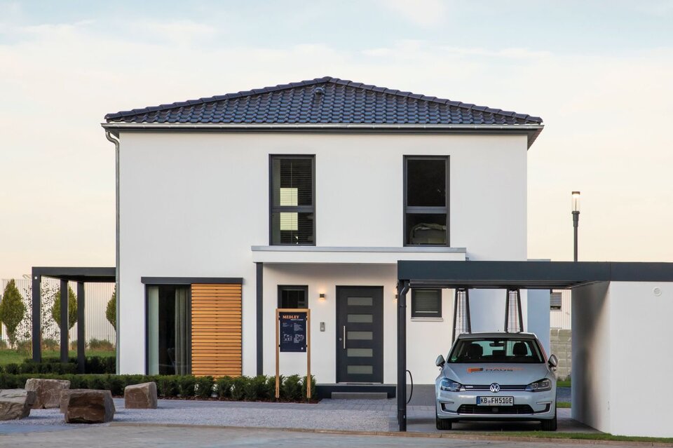 Moderne Außenansicht des FingerHaus Musterhauses MEDLEY 300 B in Frankenberg mit weißer Fassade, Walmdach, Carport und klarer Architektur.