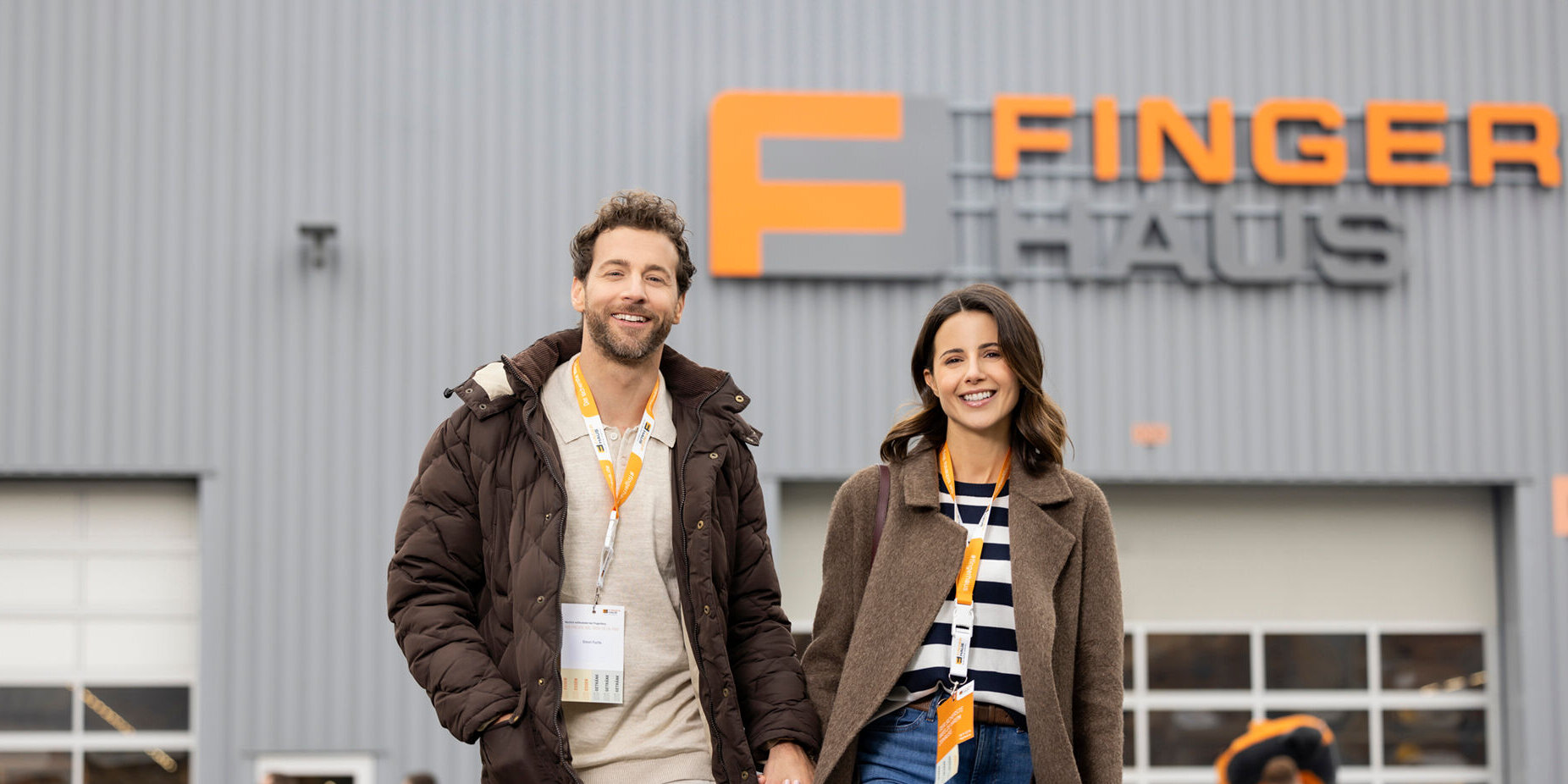 Ein Paar geht lächelnd über das Veranstaltungsgelände des FingerHaus-Bauinfotags in Frankenberg. Im Hintergrund ist eine Halle mit dem FingerHaus-Logo zu sehen, umgeben von weiteren Besuchern.