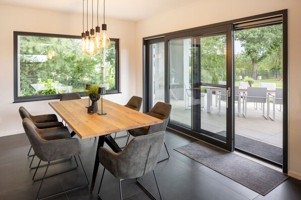 Moderner Essbereich mit Holztisch und stilvollen Stühlen, große Fensterfront mit Zugang zur Terrasse.