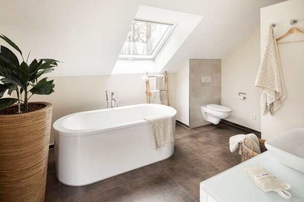 Helles Badezimmer im Musterhaus NEO 312 in Bad Vilbel mit moderner freistehender Badewanne, Dachfenster und stilvollen Naturakzenten.
