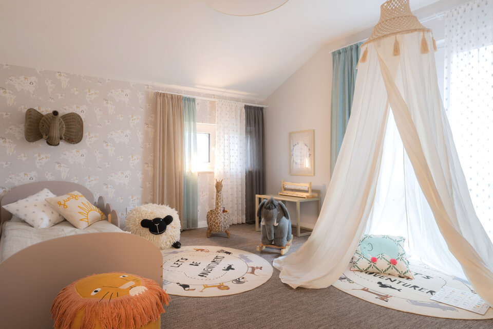 Verspieltes Kinderzimmer mit Bett, Baldachin und runden Teppichen. Weiche Farben, Tierdekoration und Licht von großen Fenstern schaffen eine warme, freundliche Atmosphäre im Musterhaus SENTO Bad Vilbel.