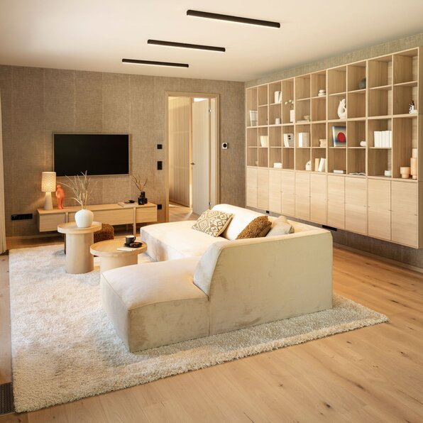 Wohnzimmer im FingerHaus Musterhaus NIVO in Frankenberg mit hellem Ecksofa, großem Wandregal aus Holz, Fernseher und zwei runden Couchtischen.