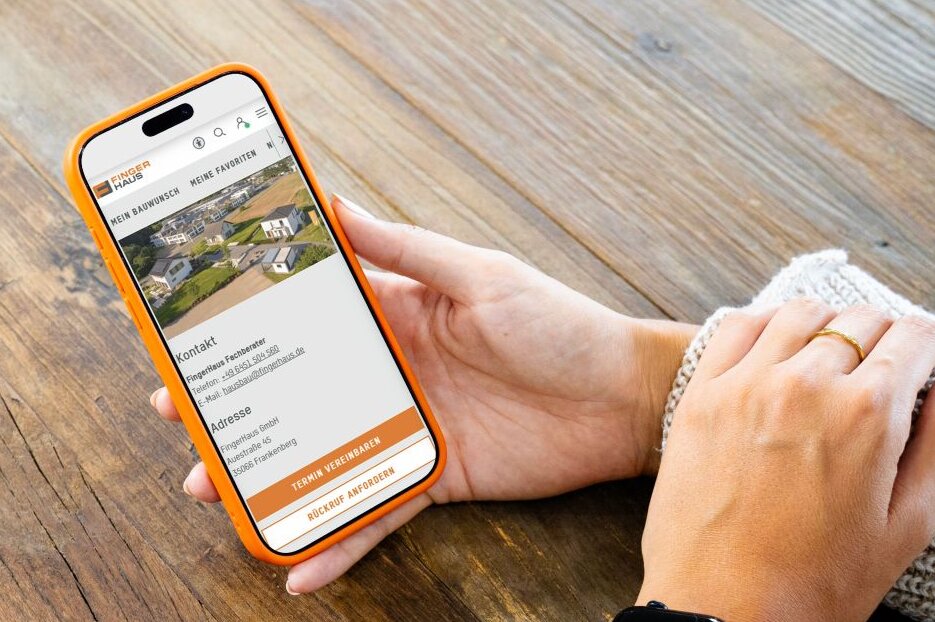 Person hält ein Smartphone mit dem FingerHaus+-Account in den Händen. Auf dem Display sind Kontaktdaten und Informationen zur gezielten persönlichen Beratung für Bauinteressierte zu sehen.