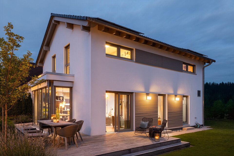 Abendliche Außenansicht des FingerHaus-Musterhauses MEDLEY in München-Poing mit beleuchteter Terrasse, großen Fensterflächen und moderner Architektur.
