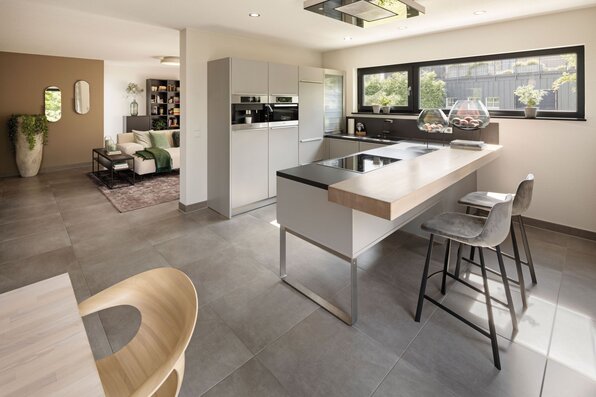 Moderne Küche im FingerHaus Musterhaus NEO 300 in Hannover mit Kochinsel, Frühstückstheke, großen Fenstern und offenem Übergang ins Wohnzimmer.