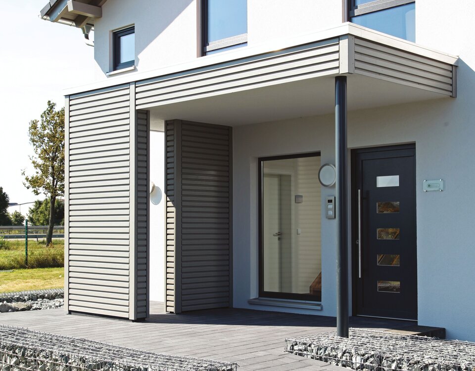 Eingangsbereich des FingerHaus Musterhauses NEO 300 in Hannover mit moderner Überdachung, klarer Architektur und Gabionenmauer.