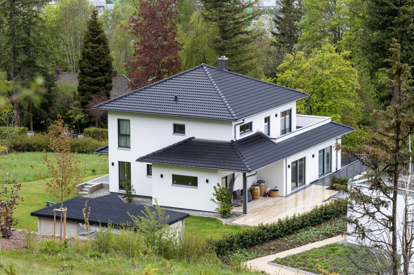 Modernes frei geplantes FingerHaus mit weißer Fassade und dunklem Walmdach, eingebettet in grüne Natur und Gartenlandschaft.