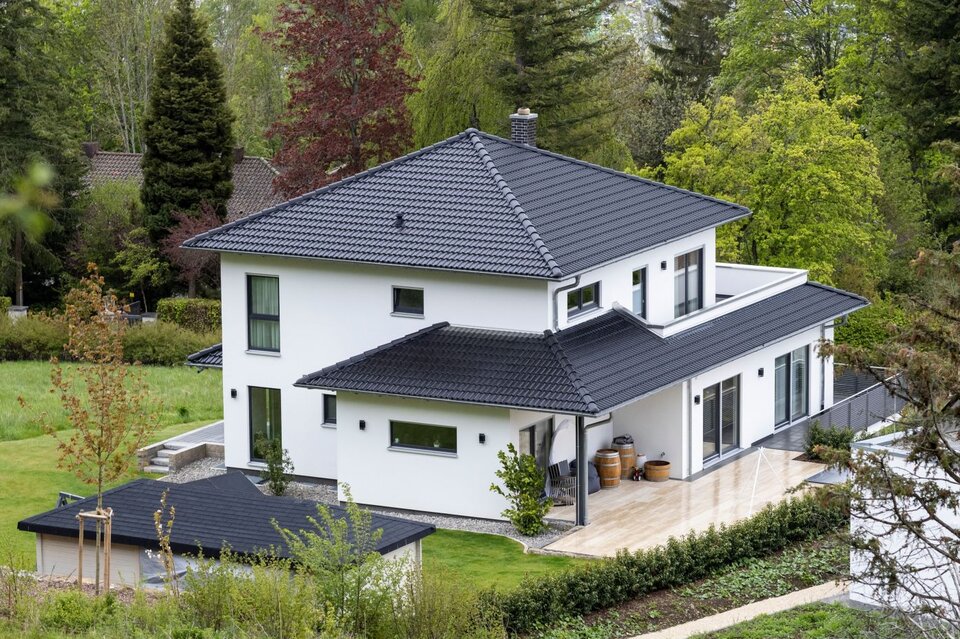 Modernes frei geplantes FingerHaus mit weißer Fassade und dunklem Walmdach, eingebettet in grüne Natur und Gartenlandschaft.