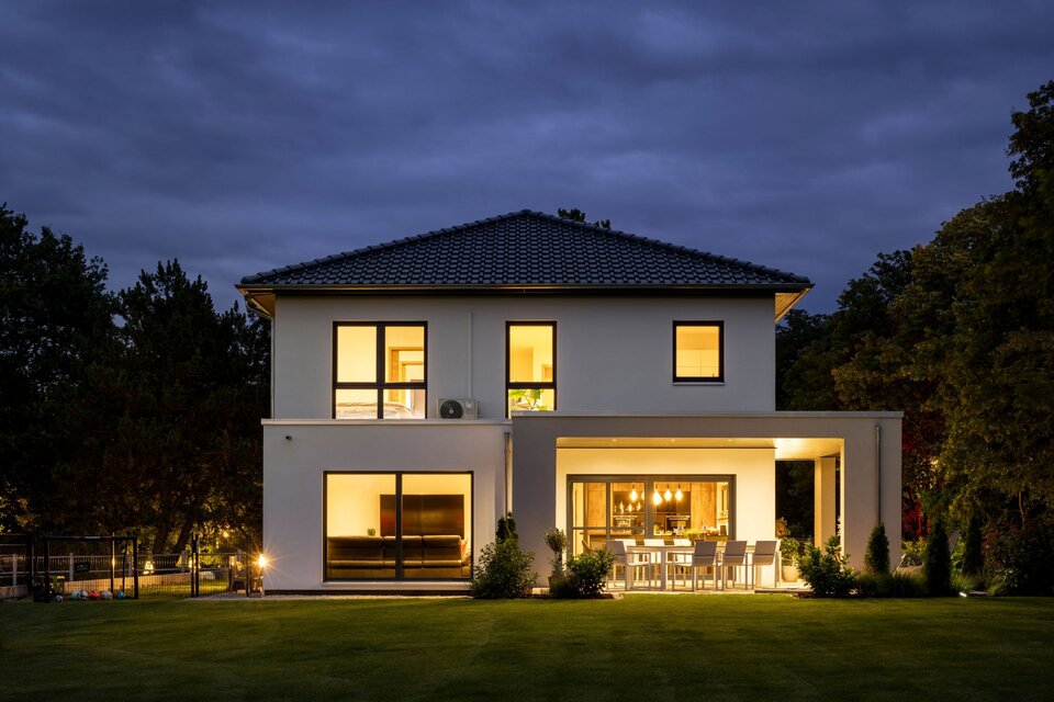 Modernes zweigeschossiges FingerHaus bei Nacht mit stimmungsvoller Beleuchtung und überdachter Terrasse.