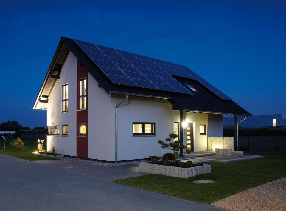 Musterhaus VIO 400 in Köln bei Nacht, mit beleuchtetem Eingangsbereich und großflächiger Photovoltaikanlage auf dem Dach.