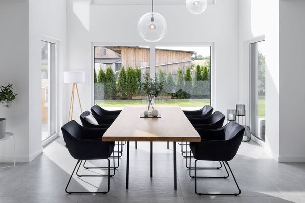 Heller Essbereich in einem modernen FingerHaus mit großem Holztisch, schwarzen Stühlen und bodentiefen Fenstern. Minimalistisches Design mit viel Tageslicht.