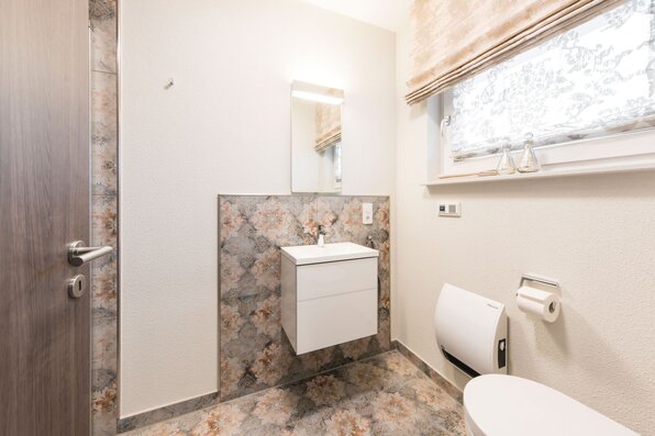 Gästebad im FingerHaus MEDLEY 300 B Musterhaus Berlin/Werder mit floraler Fliesenoptik, Waschtisch und WC.