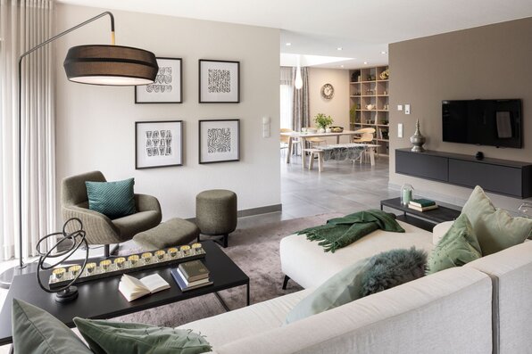 Modernes Wohnzimmer im FingerHaus NEO 300 Musterhaus in Hannover mit hellen Sofas, grünem Sessel, stilvoller Wanddekoration und offenem Essbereich.