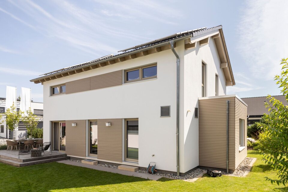 Moderne Rückansicht des Musterhauses MEDLEY 300 B in Poing mit großer Terrasse, gepflegtem Garten und klarer Linienarchitektur.