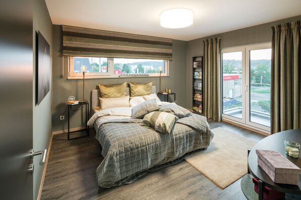 Modern eingerichtetes Schlafzimmer im FingerHaus MEDLEY 300 B Musterhaus Kassel mit Doppelbett, großen Fenstern und stimmiger Beleuchtung.