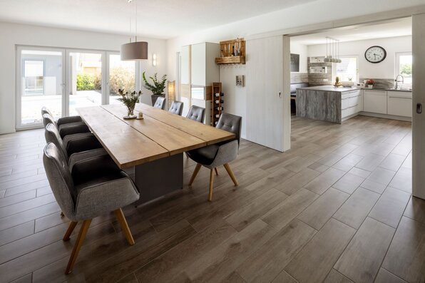 Offener Essbereich mit großem Holztisch und angrenzender moderner Küche in einem frei geplanten Finger-Haus.