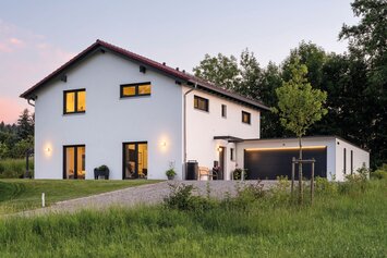 Zweigeschossiges Wohnhaus mit beleuchteten Fenstern und großem Garten bei Abenddämmerung.