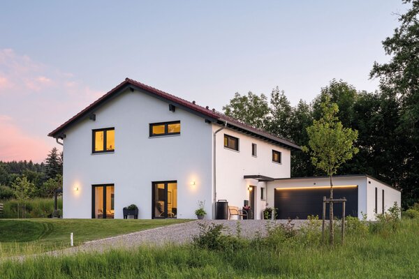 Zweigeschossiges Wohnhaus mit beleuchteten Fenstern und großem Garten bei Abenddämmerung.