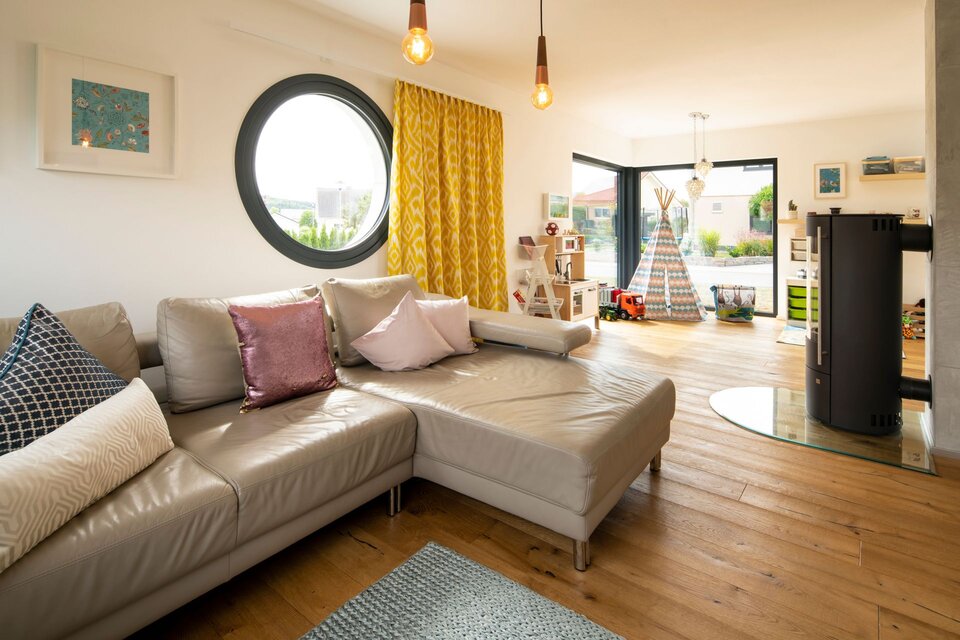 Helles Wohnzimmer mit Rundfenster, Leder-Ecksofa und offenem Wohnbereich.