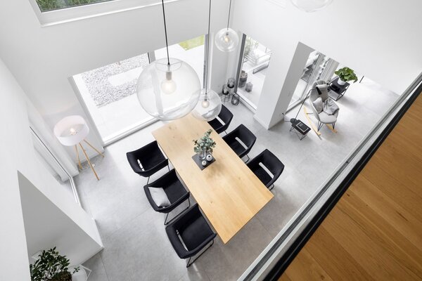 Heller Essbereich eines modernen FingerHaus mit großem Holztisch, schwarzen Stühlen und bodentiefen Fenstern. Offene Galerie sorgt für viel Licht und ein großzügiges Raumgefühl.